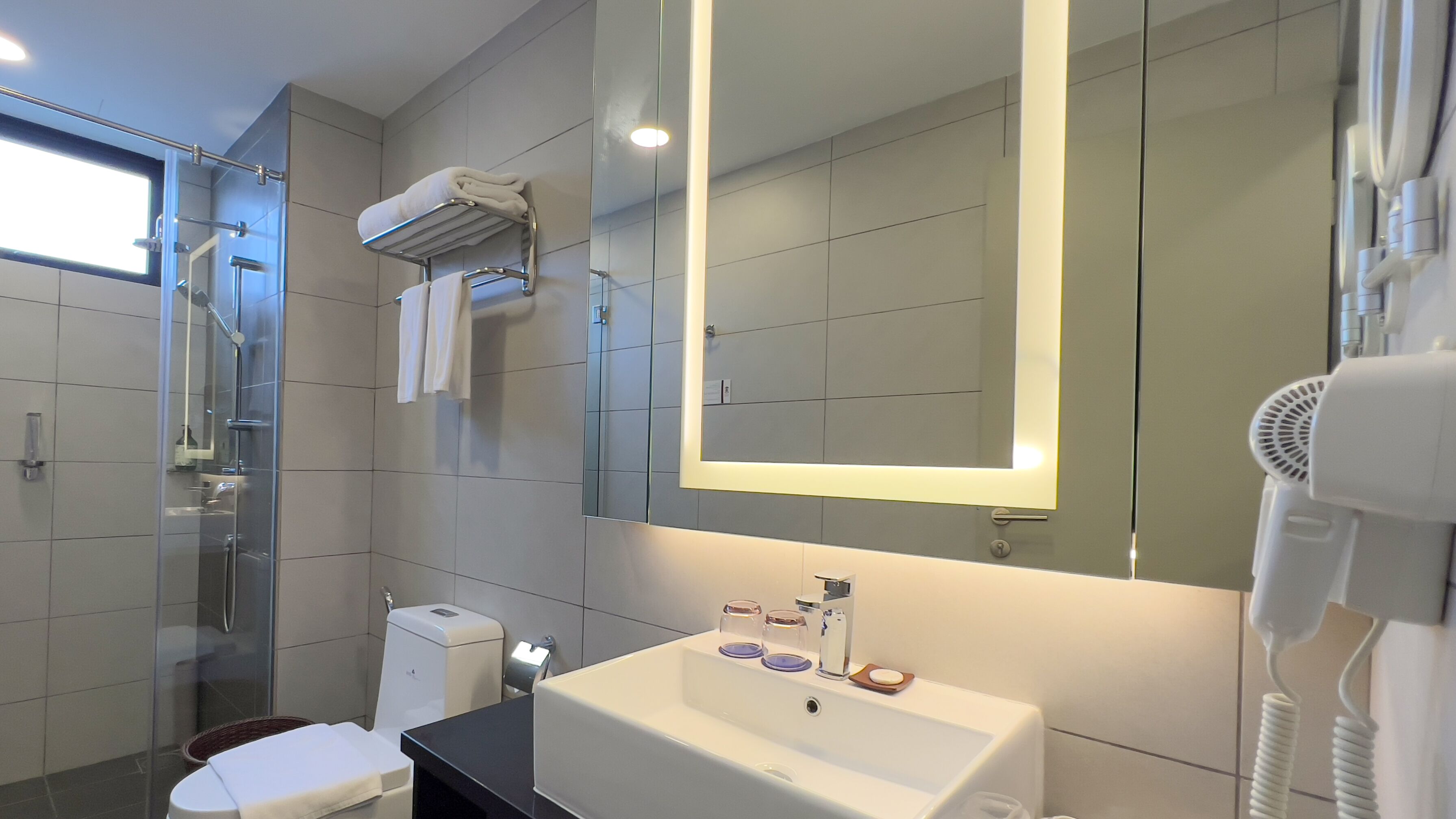 A modern bathroom with a glass shower enclosure, a white sink with a mirror above it, and a hairdryer on the right.