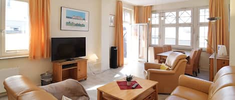 Ein modernes Wohnzimmer mit Ledersofas, einem Holztisch, einem Flachbildfernseher und einem Essbereich mit Tisch und Stühlen.