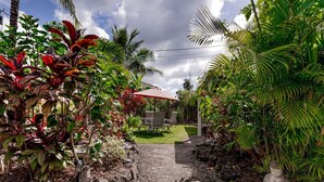 Un sendero de jardín conduce a una zona de estar con una mesa y sillas, rodeada de exuberante vegetación tropical y una estatua de Buda.