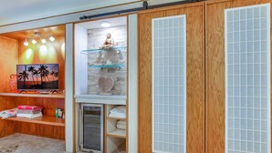 Una habitación con un televisor sobre una repisa de madera, una estatua sobre una repisa de vidrio y un refrigerador.