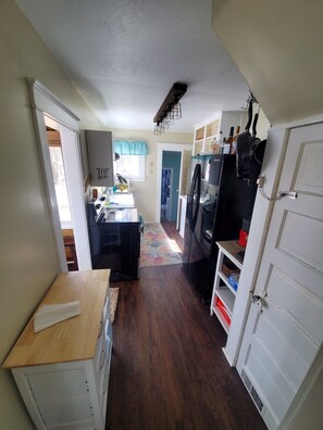 A compact kitchen with a refrigerator, stove, and cabinets. A wooden table and a rug are visible.