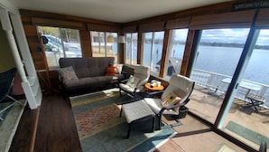 Une pièce chaleureuse avec un canapé, deux fauteuils et un tapis. De grandes fenêtres offrent une vue sur le lac et les bateaux.