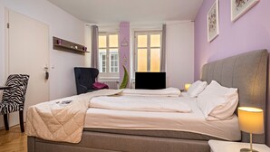 A bedroom with a bed, bedside table, lamp, chair, and a window with curtains. - Apartment 'Seenaah Lindau 9' 3 Minutes from the Lake with Wi-Fi, No Kitchen (Lindau)