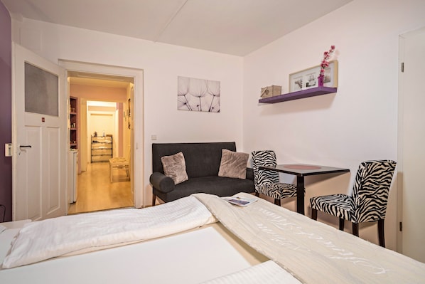A room with a bed, a sofa, a table, and zebra-patterned chairs.