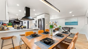 Een moderne keuken met een centraal eiland, een houten eettafel met zwarte placemats en oranje stoelen.