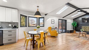 Een moderne keuken met witte kasten, een eethoek met een ronde tafel en gele stoelen, en een plafondventilator.