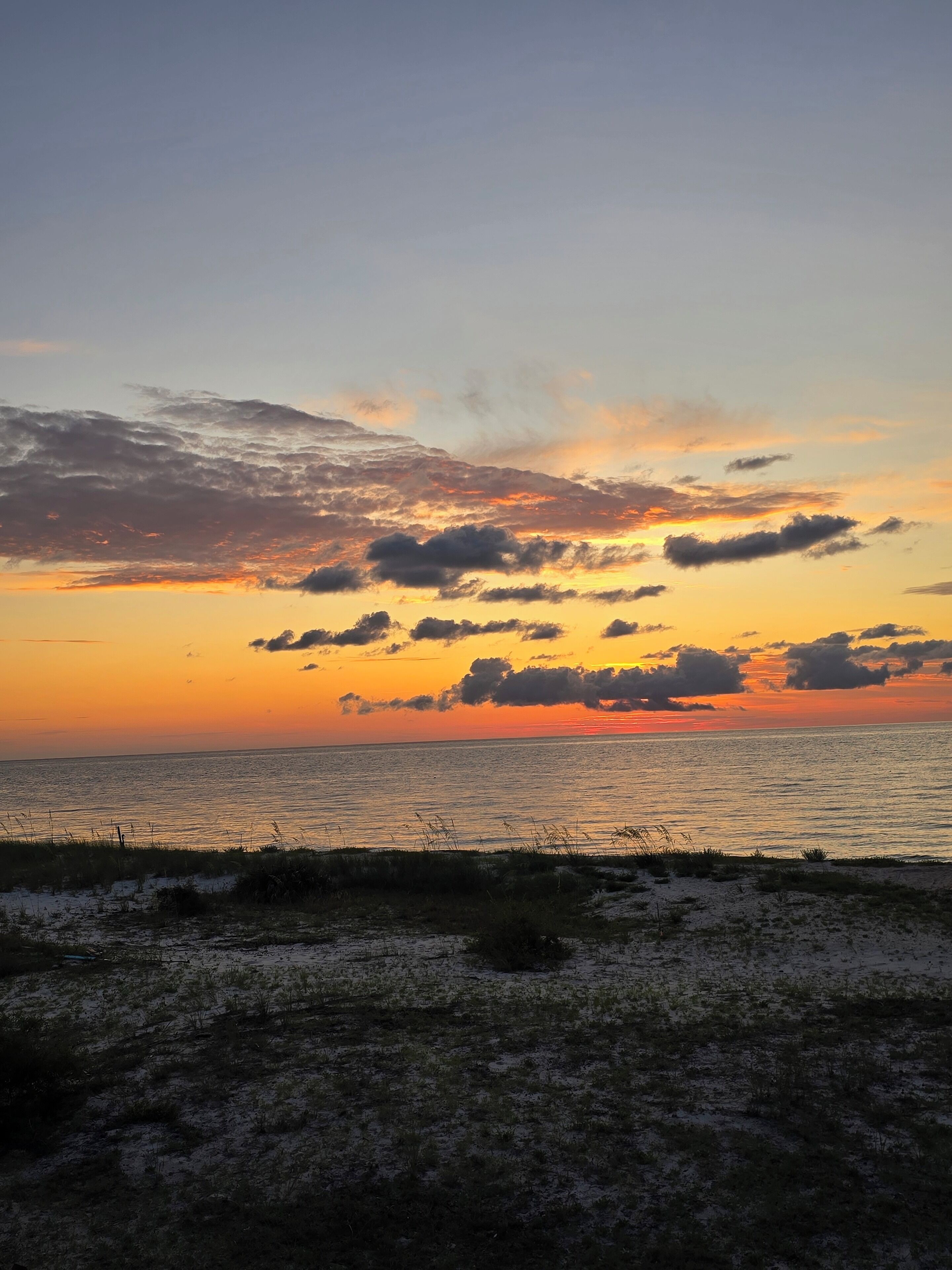 A beach at sunset with a clear sky and calm sea.