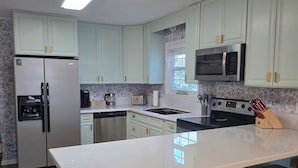A modern kitchen with light green cabinets, a stainless steel refrigerator, a microwave, a stove, and a large island with stools. - Beach Getaway Just Refreshed, Sleeps 8 <4 br> EV level 2 charging- views (Alligator Point)