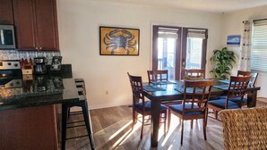 A dining area with a wooden table and chairs, a kitchen with a microwave and coffee maker, and a framed artwork on the wall. - Beach Getaway Just Refreshed, Sleeps 8 <4 br> EV level 2 charging- views (Alligator Point)