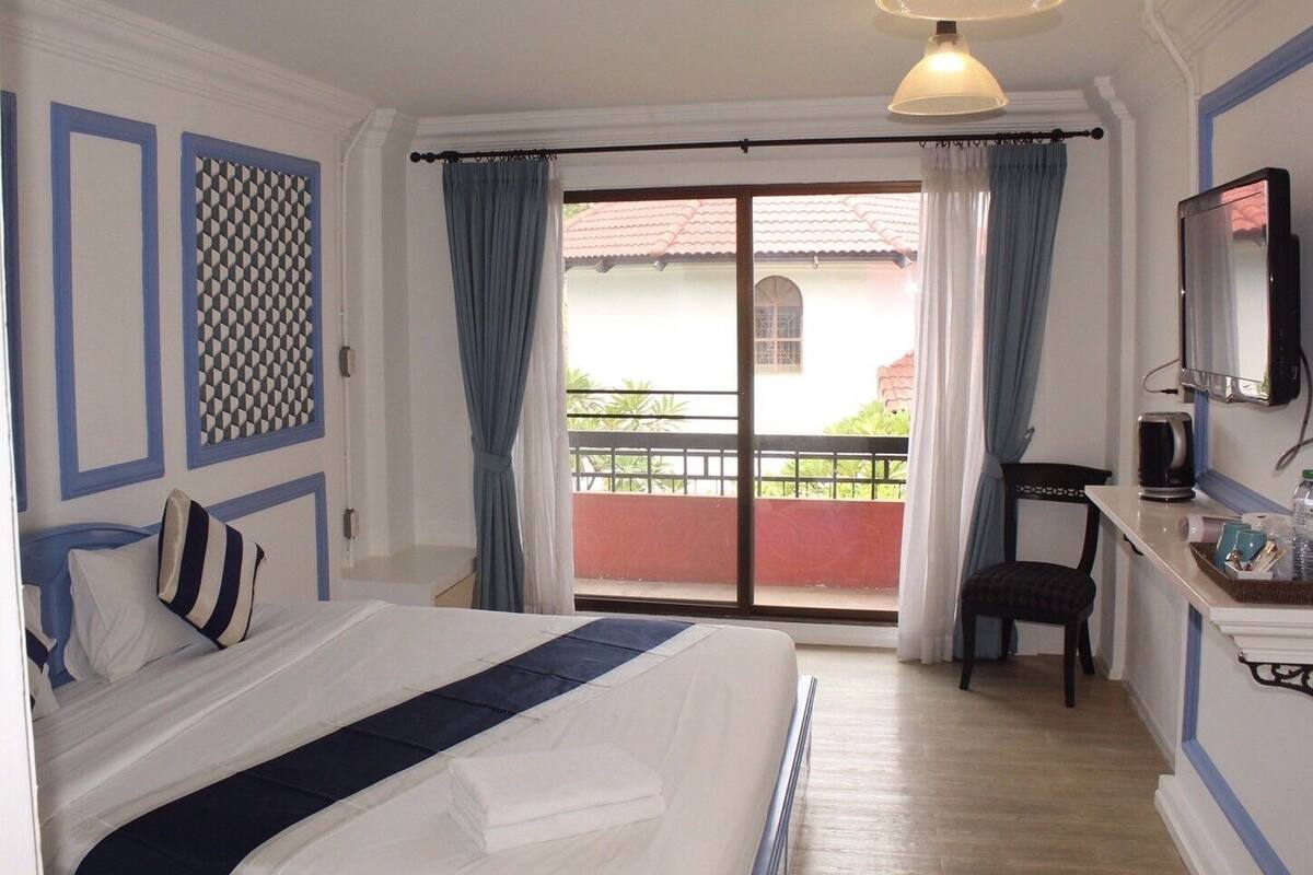 Een hotelkamer met een bed, een bureau met stoel, een televisie en een balkon met gordijnen.