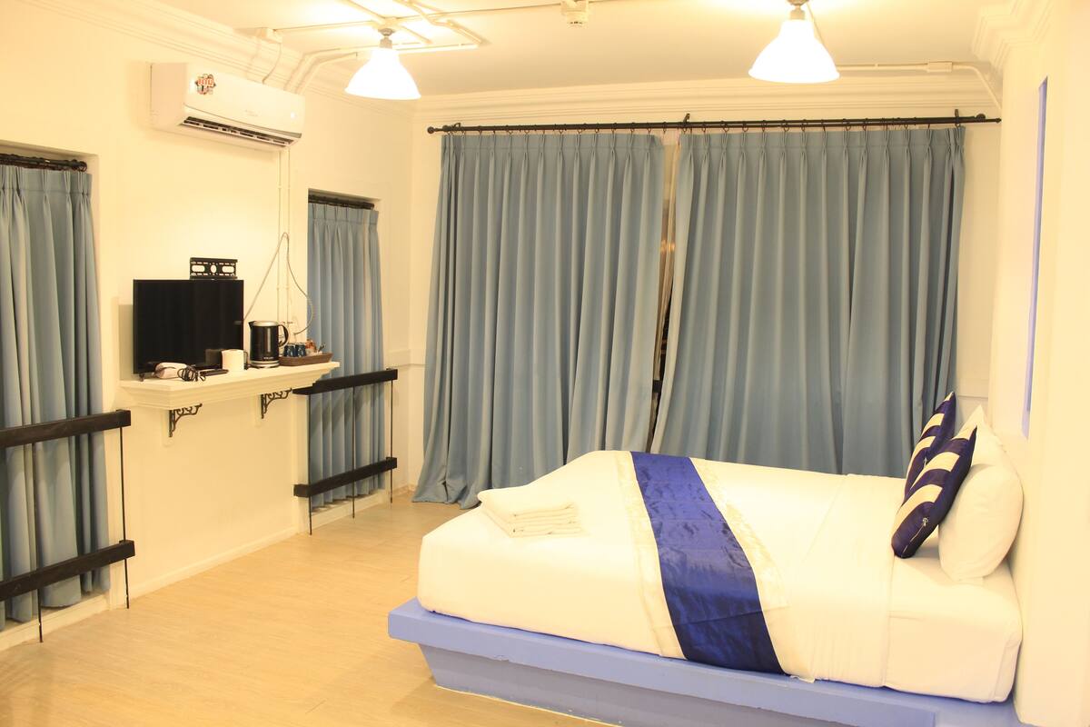 Een slaapkamer met een bed, een bureau met een computer en een raam met gordijnen.