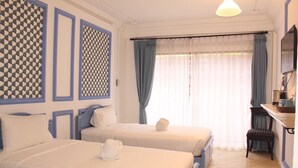 A hotel room with two beds, a desk, a chair, and a large window with curtains. - Kudos Boutique Hotel (Pattaya)