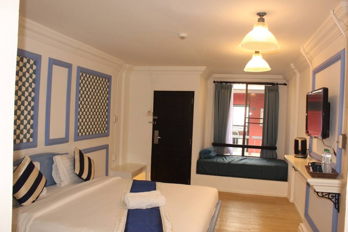 Een hotelkamer met een bed, een bureau met computer, een raam met gordijnen en een televisie aan de muur.