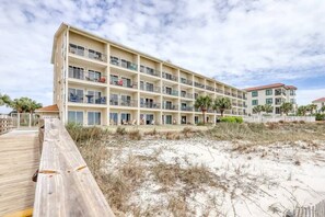 Ein mehrgeschossiges Hotel mit Balkonen, einem Holzsteg und einem Sandstrand.