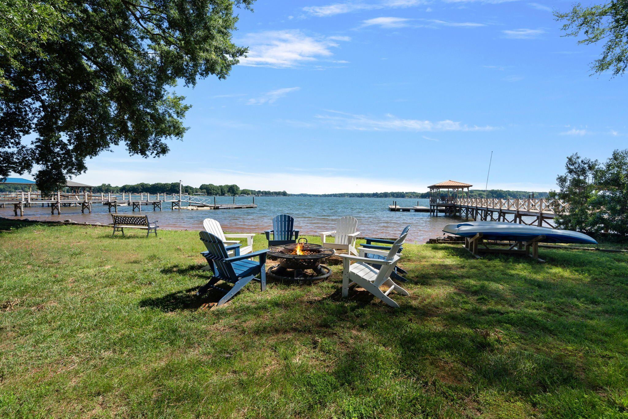 A lakeside outdoor seating area with Adirondack chairs, a fire pit, and a canoe.