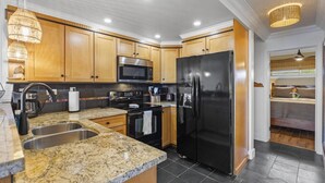 A modern kitchen with granite countertops, stainless steel appliances, and wooden cabinets. - Ocean-View Condo in the Heart of Kona | Walk to Shops, Beaches & Dining (Kailua-Kona)