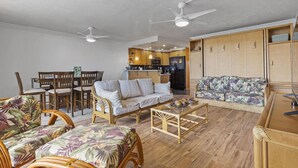 A spacious living area with a dining set, a sofa, and a kitchen in the background. - Ocean-View Condo in the Heart of Kona | Walk to Shops, Beaches & Dining (Kailua-Kona)