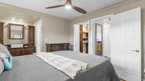 A bedroom with a bed, a ceiling fan, a dresser, a mirror, and a walk-in closet. - Ocean-View Condo in the Heart of Kona | Walk to Shops, Beaches & Dining (Kailua-Kona)