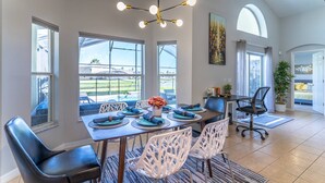 A dining area with a table set for four, large windows, and a view of the outdoors. - Single-Story Pool Home | Water Views & Game Room | Sleeps 11 (Kissimmee)