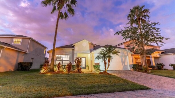 A residential house with a well-maintained lawn, palm trees, and a paved driveway. - Single-Story Pool Home | Water Views & Game Room | Sleeps 11 (Kissimmee)