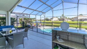 A covered outdoor area with a pool, seating, and a view of the surrounding landscape. - Single-Story Pool Home | Water Views & Game Room | Sleeps 11 (Kissimmee)
