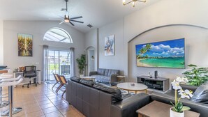 A spacious living area with a large window, a ceiling fan, a flat-screen TV, and a sofa. - Single-Story Pool Home | Water Views & Game Room | Sleeps 11 (Kissimmee)