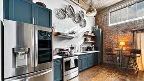 Een moderne keuken met roestvrijstalen apparatuur, een bakstenen muur en een eethoek met een tafel en stoelen.