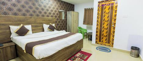 A hotel room with a wooden bed, a green chair, a trash bin, and a patterned rug.
