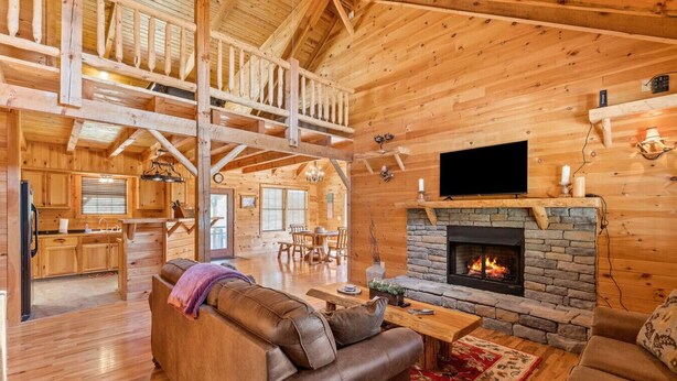 A log cabin interior with a stone fireplace, wooden furniture, and a dining area. - Starry Mountain Night | Seasonal Private Pool + Pool Table, Kid`s Playset (Stanton)