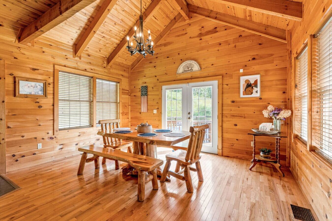 L’intérieur d’un chalet en bois comprend une table à manger, des chaises, un lustre et une petite étagère ornée de fleurs.