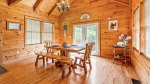 A wooden cabin interior with a dining table, chairs, a chandelier, and a small shelf with flowers. - Starry Mountain Night | Seasonal Private Pool + Pool Table, Kid`s Playset (Stanton)