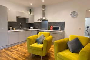 A modern kitchen with a microwave, kettle, and sink. There are two yellow armchairs with cushions. - De Parys Flat 1 in Bedford (Bedford)