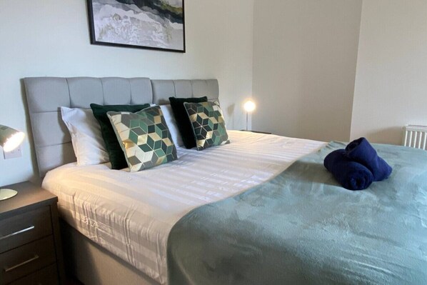 Un lit bien fait, agrémenté d’un coussin à motifs géométriques, d’une couverture bleue et d’une tête de lit.