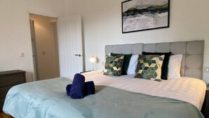 Une chambre d’hôtel avec un lit, une porte, une table de chevet et une lampe fixée au mur.