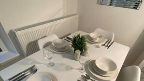 A dining table set with white plates, cutlery, and glasses, with a small plant centerpiece.