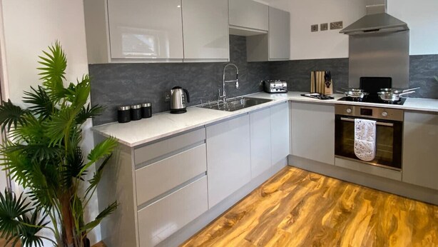 A modern kitchen with white cabinets, a stainless steel range hood, a built-in oven, and a wooden floor.