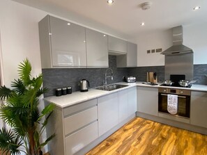 A modern kitchen with white cabinets, a stainless steel range hood, a built-in oven, and a wooden floor. - De Parys Serviced Flat in Bedford 4 (Bedford)