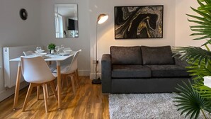 A modern living room with a dark grey sofa, a dining table with chairs, a large abstract painting, and a floor lamp.