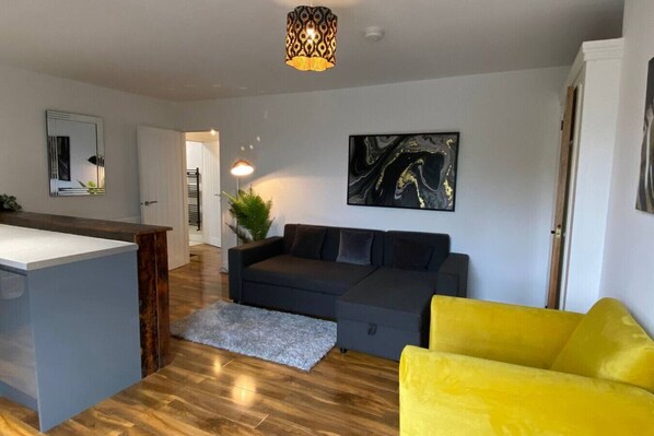 A modern living room with a grey sofa, a yellow armchair, a black abstract painting, and a wooden floor.