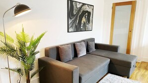A modern living room with a grey sectional sofa, a floor lamp, a potted plant, and a piece of abstract art on the wall. - Spacious 2BR Bradford Home for 6 (Bedford)