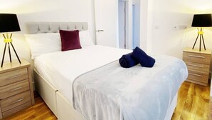 A hotel room with a bed, two bedside tables with lamps, a door, and a wooden floor. - Spacious 2BR Bradford Home for 6 (Bedford)
