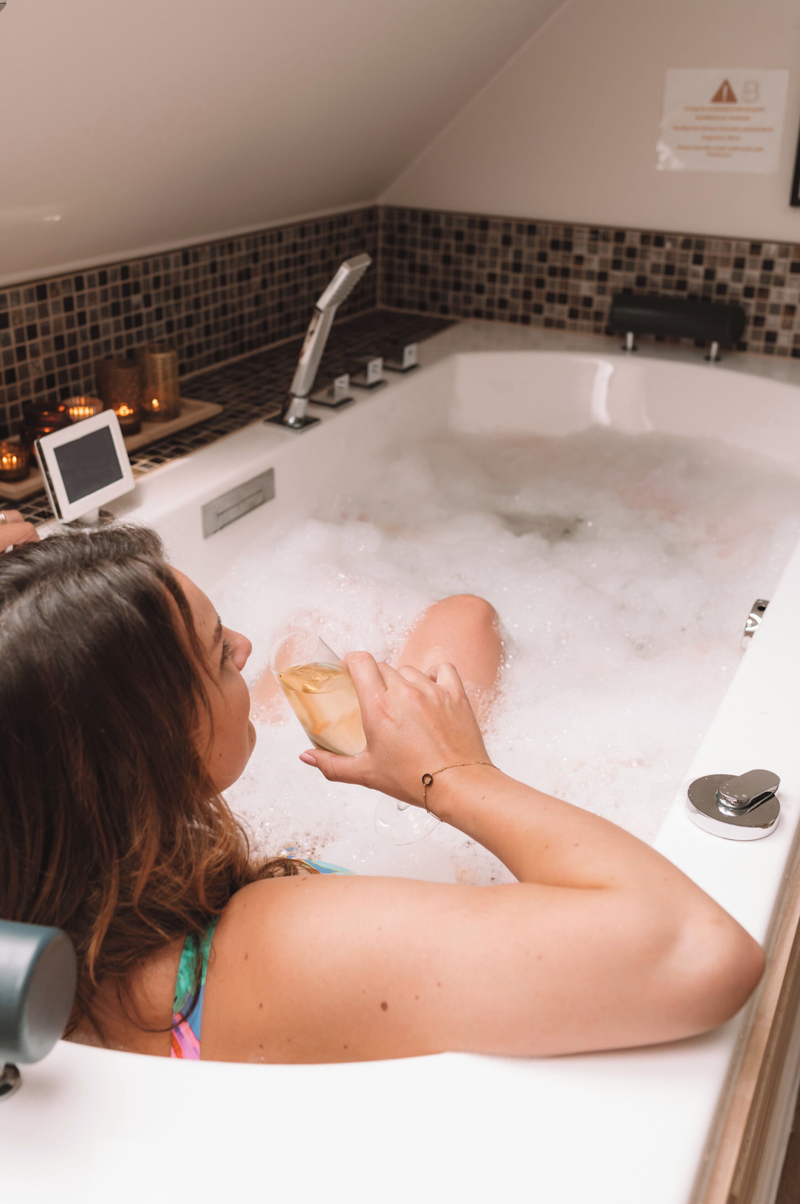 Una persona relajándose en una bañera con un teléfono inteligente y velas a un lado.