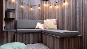 Eine Sitzecke mit gepolsterten Bänken, einem kleinen Hocker und Lichterketten an einer Holzwand.