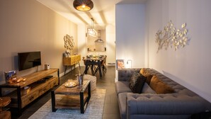 Ein modernes Wohnzimmer mit Sofa, Couchtisch, Fernseher und einem Essbereich mit Stühlen und Tisch.
