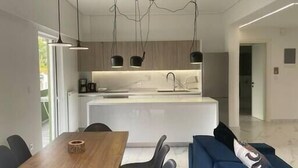 Eine moderne Küche mit Pendelleuchten, ein Essbereich mit Holztisch und -stühlen sowie ein blaues Sofa.