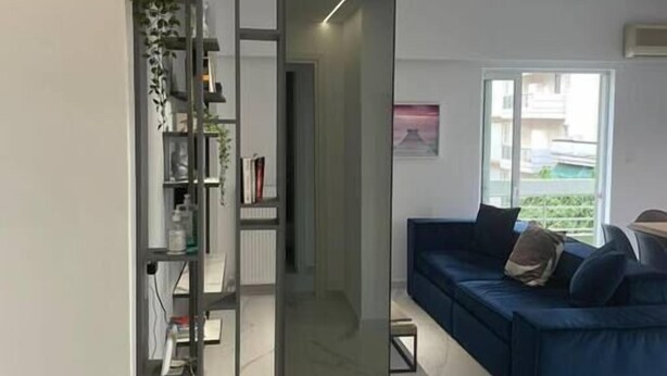 Ein modernes Wohnzimmer mit einem blauen Sofa, einer Glastrennwand und Blick ins Freie.