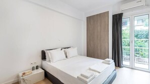 Ein modernes Schlafzimmer mit einem großen Bett, einem Nachttisch mit Büchern und Blick auf Grün durch das Fenster.