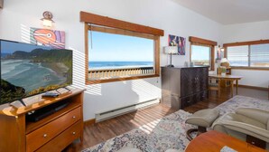 A living room with a large TV, wooden furniture, a fireplace, and a view of the ocean. - New Listing! Cozy beachfront home on famed Heceta Beach, amazing sunsets (Florence)