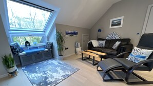 Ein modernes Wohnzimmer mit hohen Decken, einer eingebauten Sitzbank mit Kissen, einem schwarzen Ledersofa, einem Couchtisch und Blick durch ein Dachfenster.