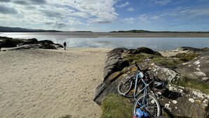 Ein Strand mit einem Fahrrad und einem Rucksack, der an einem Felsen lehnt.